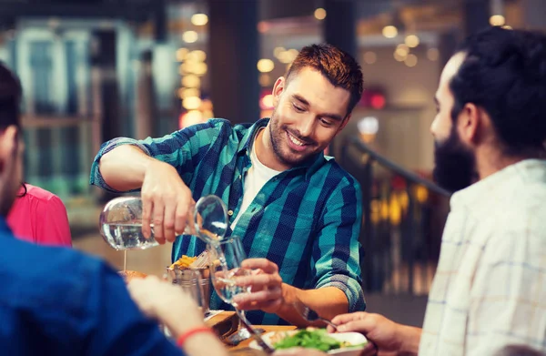 Lycklig man med vänner hälla vatten på restaurang — Stockfoto