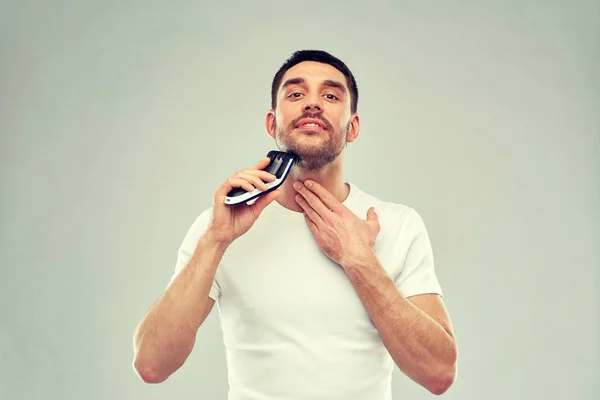 Улыбающийся мужчина бреет бороду с триммером над серой — стоковое фото