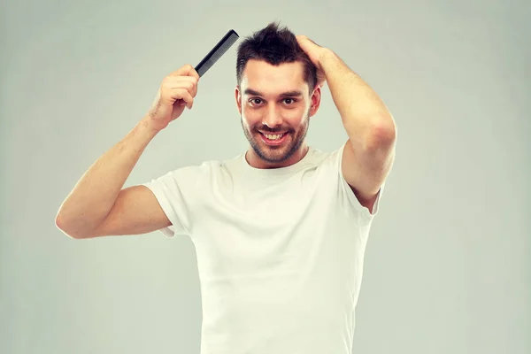 Hombre feliz cepillando el cabello con peine sobre gris — Foto de Stock