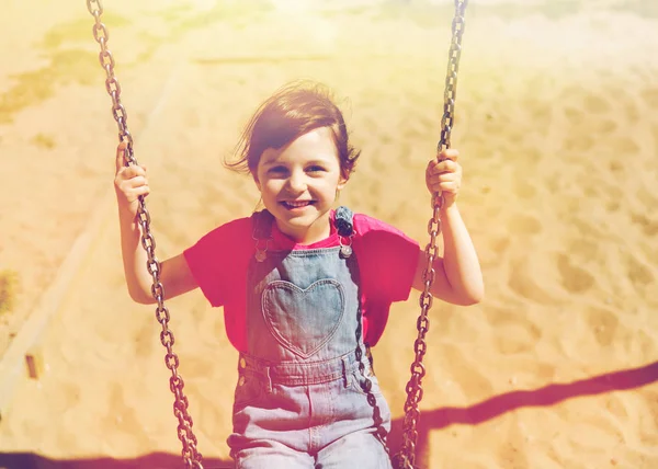 Fröhliches kleines Mädchen schaukelt auf Schaukel auf Spielplatz — Stockfoto