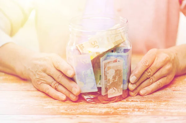 Закрывать глаза на пожилую женщину с деньгами в стеклянной банке — стоковое фото