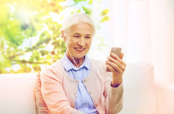 Donna anziana con smartphone e auricolari a casa — Foto Stock