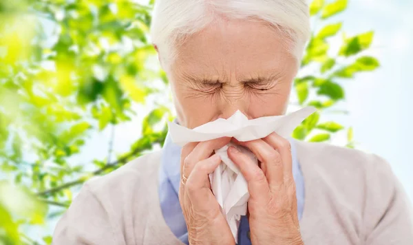 Sick senior woman blowing nose to paper napkin — Stock Photo, Image