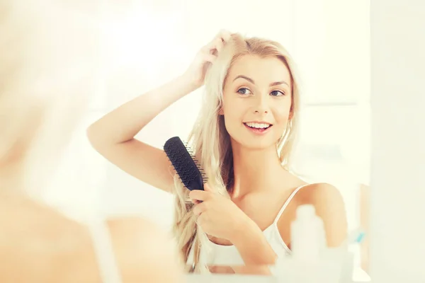 Mujer feliz cepillando el cabello con peine en el baño — Foto de Stock