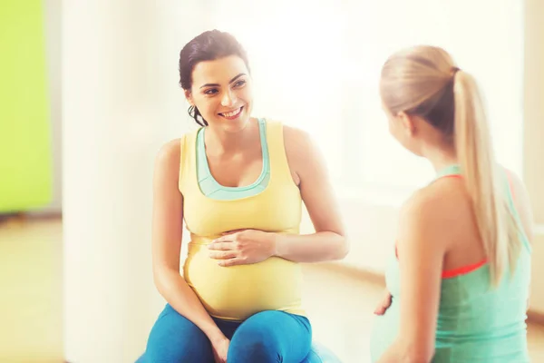 Twee gelukkige zwangere vrouwen zittend op ballen in sportschool — Stockfoto