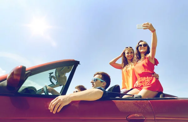 Amigos conduciendo en coche cabriolet y tomando selfie — Foto de Stock