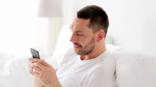 Homem com smartphone na cama em casa — Vídeo de Stock