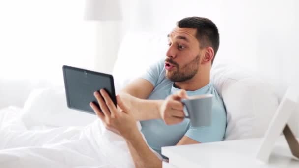 Ο άνθρωπος με το tablet pc που πίνει καφέ στο κρεβάτι στο σπίτι — Αρχείο Βίντεο