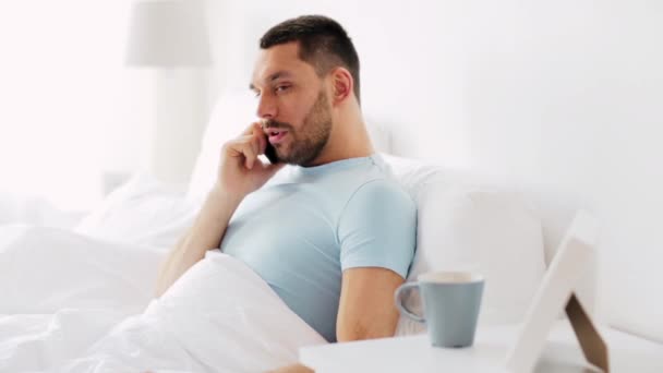 Мужчина звонит по смартфону в постели дома — стоковое видео