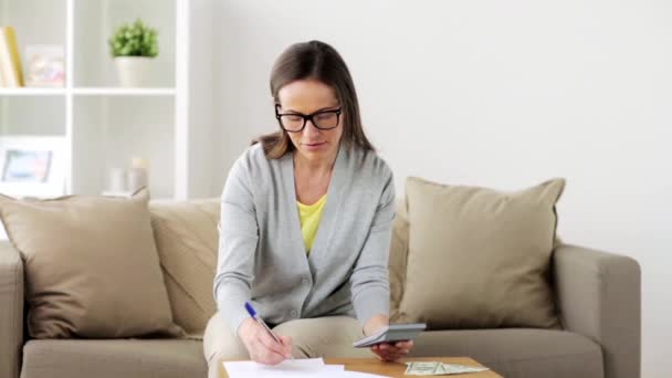 Vrouw met geld, papieren en rekenmachine thuis — Stockvideo