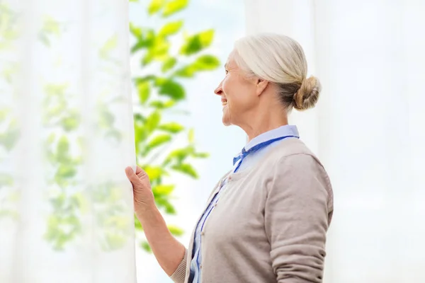 Gelukkig senior vrouw op zoek via venster thuis — Stockfoto