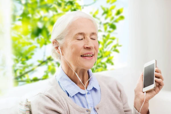 Donna anziana con smartphone e auricolari a casa — Foto Stock