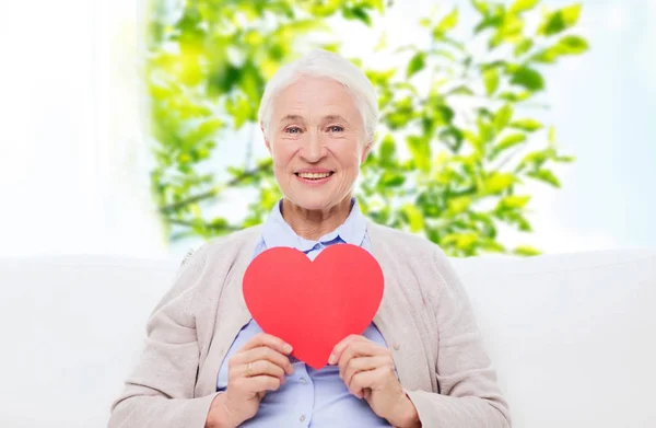 Счастливая улыбающаяся пожилая женщина с красным сердцем дома — стоковое фото