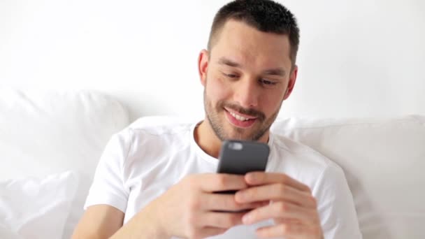 Homem com smartphone na cama em casa — Vídeo de Stock