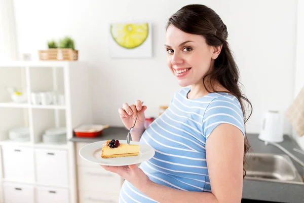 家庭の台所でケーキを食べて幸せな妊娠中の女性 — ストック写真