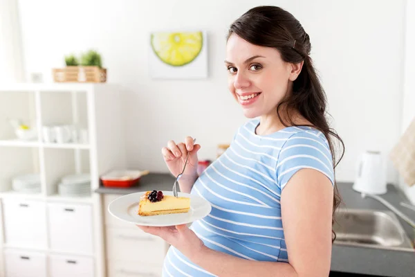 Happy pregnant woman eating cake at home kitchen — Stock Photo, Image