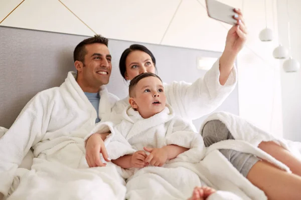 Ευτυχισμένη οικογένεια με smartphone στο κρεβάτι στο δωμάτιο του ξενοδοχείου — Φωτογραφία Αρχείου