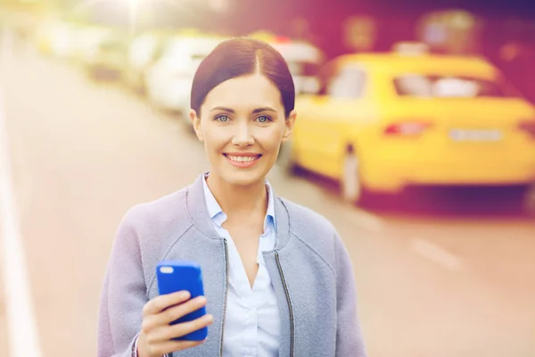 Lachende vrouw met smartphone over taxi in stad — Stockfoto