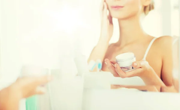 Primer plano de la mujer que aplica crema facial en el baño — Foto de Stock