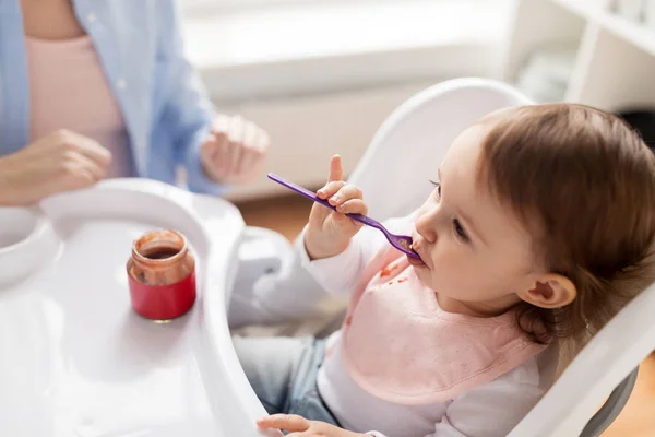 Meisje van de baby met lepel eten puree uit pot thuis — Stockfoto