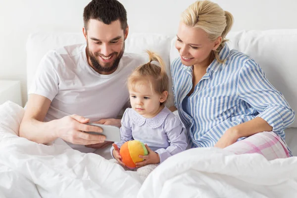 Familia feliz con teléfono inteligente en la cama en casa —  Fotos de Stock