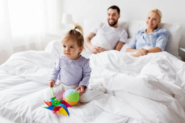 Ευτυχισμένο παιδί με τα παιχνίδια και οι γονείς στο κρεβάτι στο σπίτι — Φωτογραφία Αρχείου