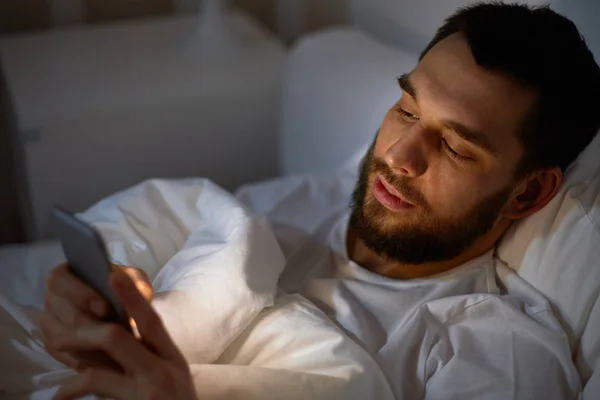 Man met smartphone in bed bij nacht — Stockfoto