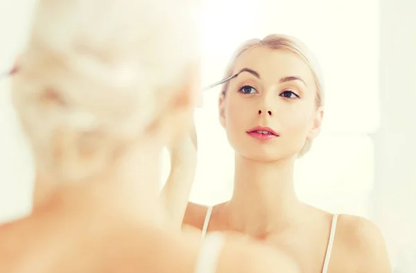 Женщина с кистью делает макияж бровей в ванной комнате — стоковое фото