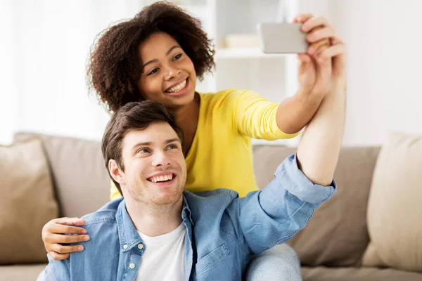 Casal feliz com smartphone levando selfie em casa — Fotografia de Stock