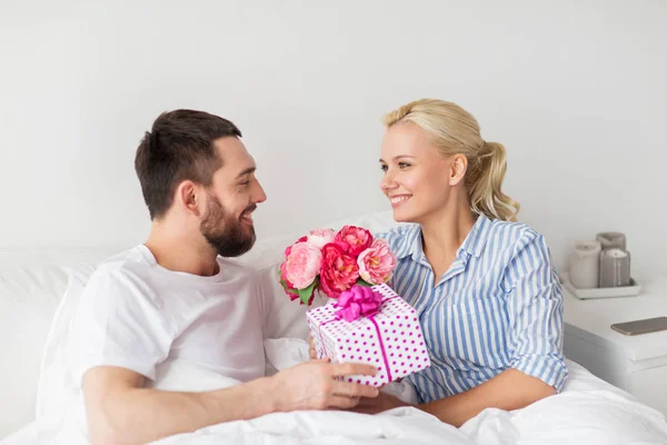 Feliz pareja con caja de regalo en cama en casa — Foto de Stock