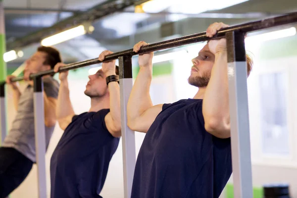 Grupo de homens jovens fazendo pull-ups no ginásio — Fotografia de Stock