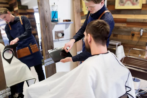 Barbero que muestra la tableta PC al hombre en la barbería —  Fotos de Stock