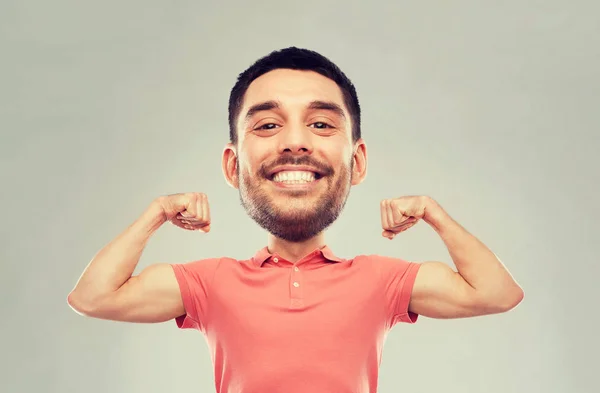 Sonriente hombre mostrando bíceps sobre fondo gris —  Fotos de Stock