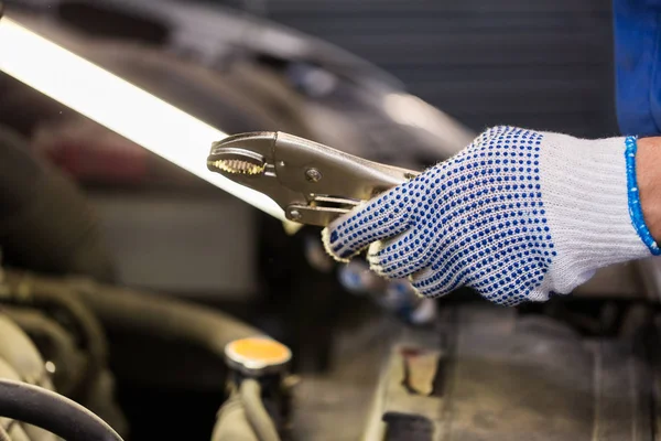 Mechanic man with pliers repairing car at workshop — Stock Photo, Image