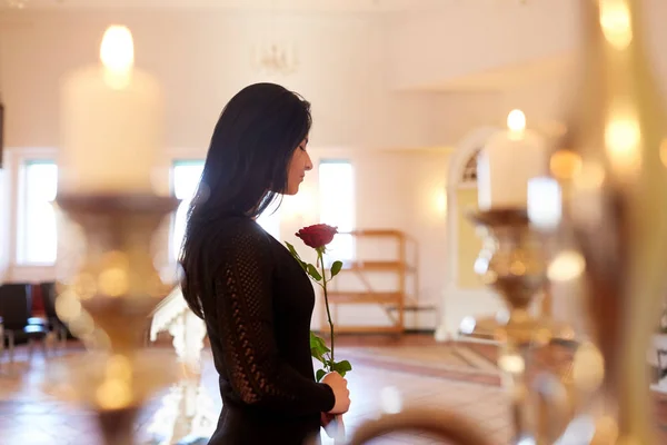 Treurige vrouw met rode roos bij begrafenis in kerk — Stockfoto