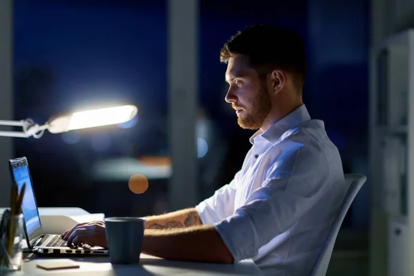 Людина з ноутбуком і кавою працює в нічному офісі — стокове фото