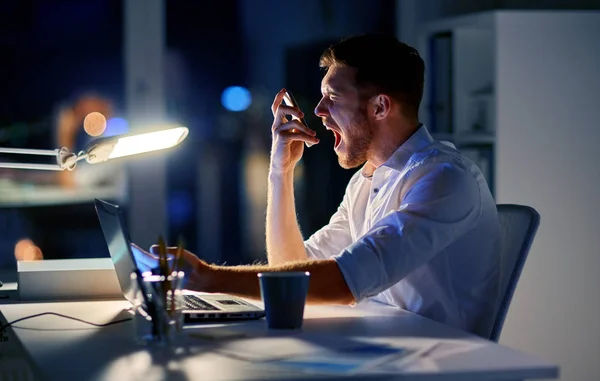 angry businessman with smartphone at night office