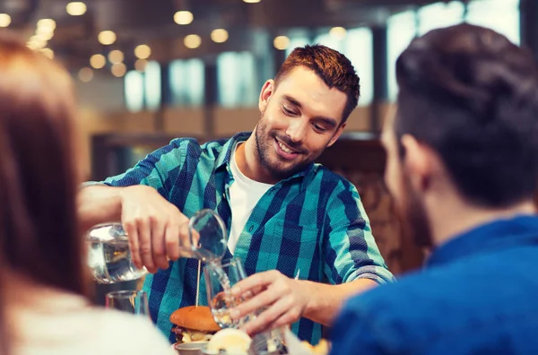 Šťastný muž s přáteli vylévá vodu v restauraci — Stock fotografie