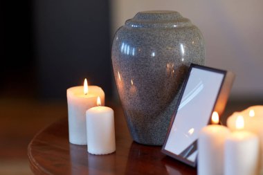 photo frame, cremation urn and candles on table clipart