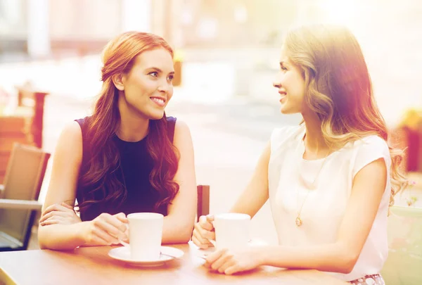 Smiling young women with coffee cups at cafe — Stock Photo, Image