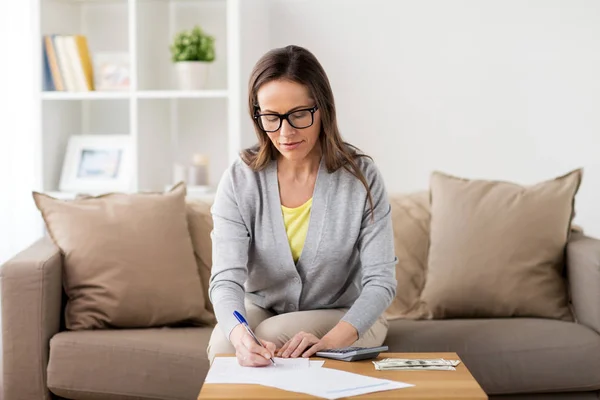 Mujer con dinero, papeles y calculadora en casa — Foto de Stock