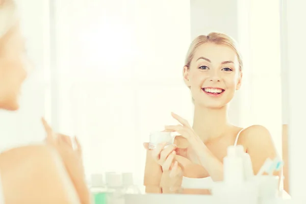 Mujer feliz aplicando crema a la cara en el baño — Foto de Stock