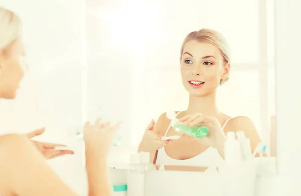 Giovane donna con lozione lavaggio viso in bagno — Foto Stock