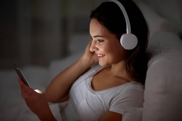 智能手机和耳机在床上的女人 — 图库照片