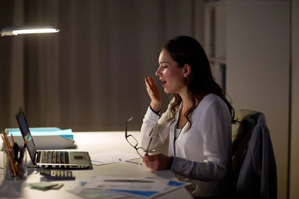 Tired woman with laptop yawning at night office — Stock Photo, Image