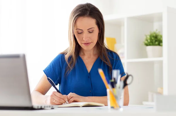 Glückliche Frau schreibt im Büro ans Notizbuch — Stockfoto