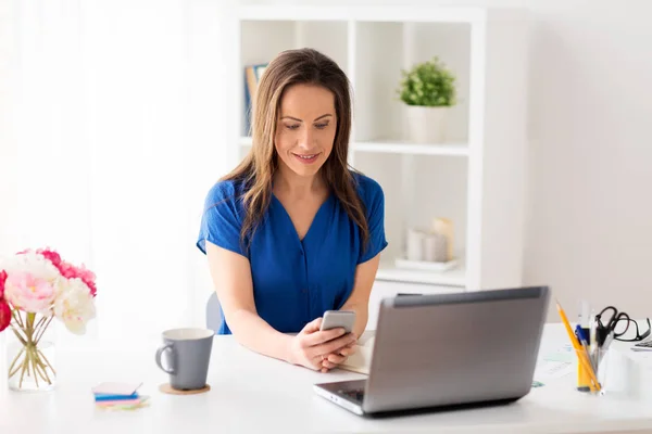 Mujer con teléfono inteligente y portátil en la oficina — Foto de Stock