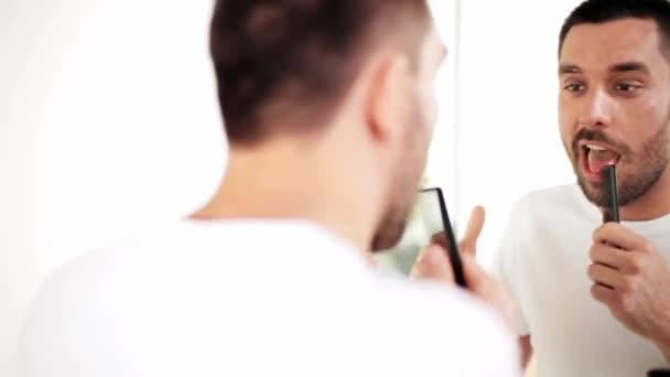 Man with comb looking to mirror and singing — Stock Video