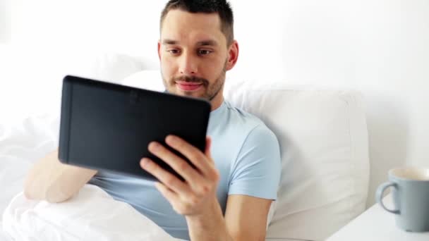 Man with tablet pc drinking coffee in bed at home — Stock Video