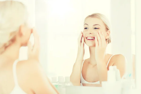 Happy woman applying cream to face at bathroom — Stock Photo, Image